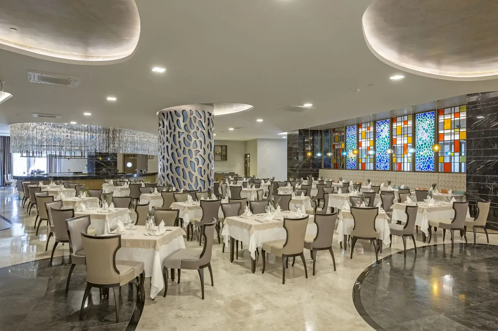 Restaurantzaal met gedekte tafels, een marmeren vloer en kleurrijke glas-in-loodramen bij Royal Seginus in Lara